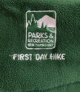 close-up of a New Hampshire State Parks "First Day Hike" logo on dark green fleece scarf