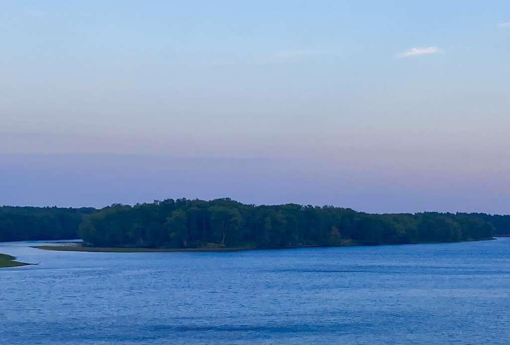 wide river, forested island, pastel-colored sky at sunset